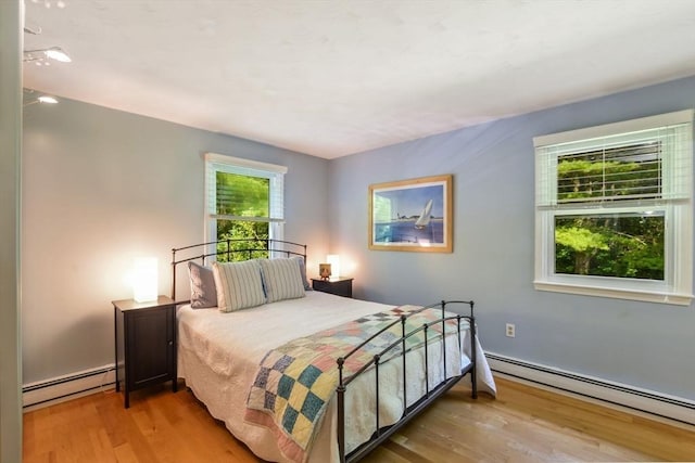 bedroom with multiple windows, a baseboard heating unit, and wood-type flooring