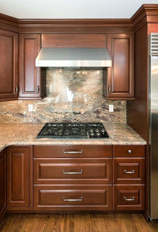 kitchen with wall chimney range hood, backsplash, gas cooktop, and stainless steel refrigerator