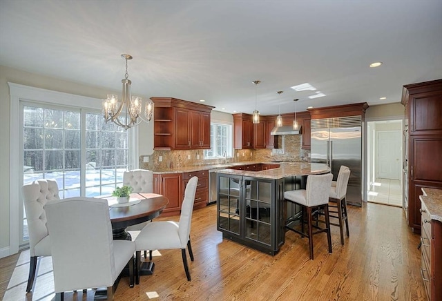 kitchen featuring decorative light fixtures, a center island, stainless steel appliances, wall chimney range hood, and light hardwood / wood-style flooring