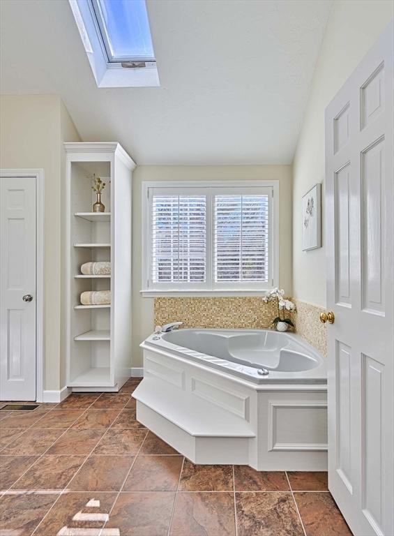 bathroom with a washtub and vaulted ceiling with skylight