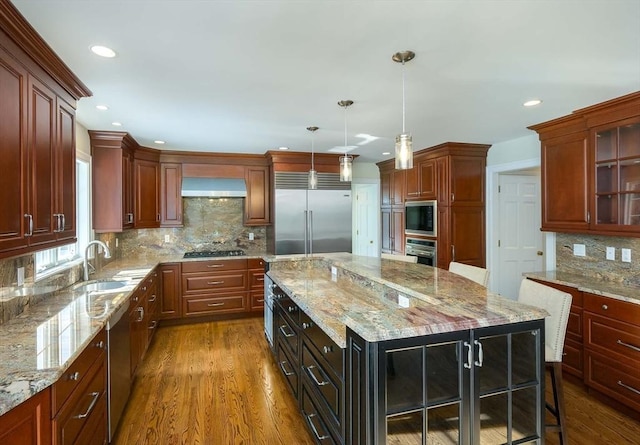 kitchen featuring hanging light fixtures, a center island, black appliances, light stone countertops, and wall chimney exhaust hood