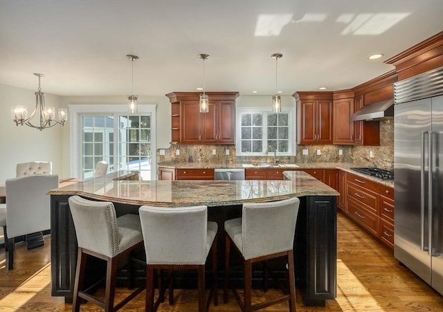 kitchen featuring appliances with stainless steel finishes, sink, hanging light fixtures, a large island, and wall chimney exhaust hood