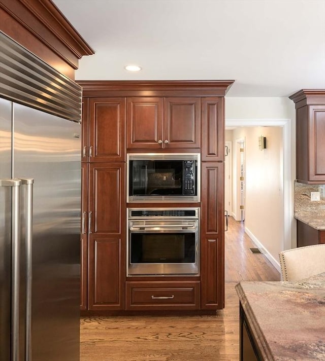 kitchen featuring light stone countertops, built in appliances, and light wood-type flooring