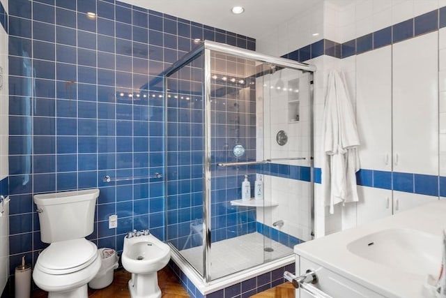 bathroom with tile walls, a shower with shower door, and a bidet