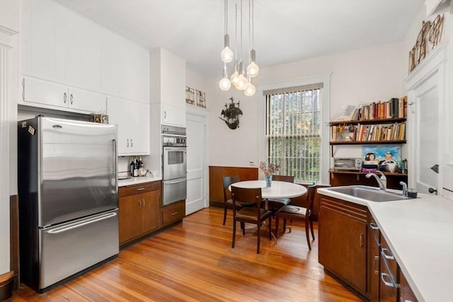 kitchen featuring white cabinetry, appliances with stainless steel finishes, sink, light hardwood / wood-style flooring, and decorative light fixtures