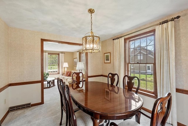 carpeted dining area with an inviting chandelier, baseboards, wallpapered walls, and visible vents