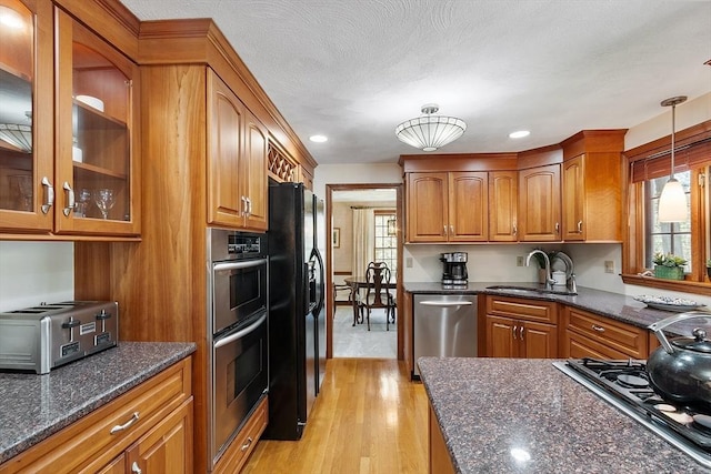 kitchen with brown cabinetry, appliances with stainless steel finishes, hanging light fixtures, a sink, and a toaster