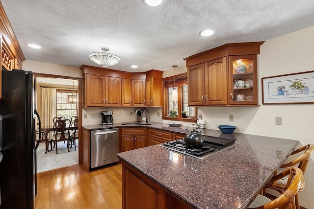kitchen with brown cabinetry, appliances with stainless steel finishes, light wood-type flooring, a sink, and a peninsula