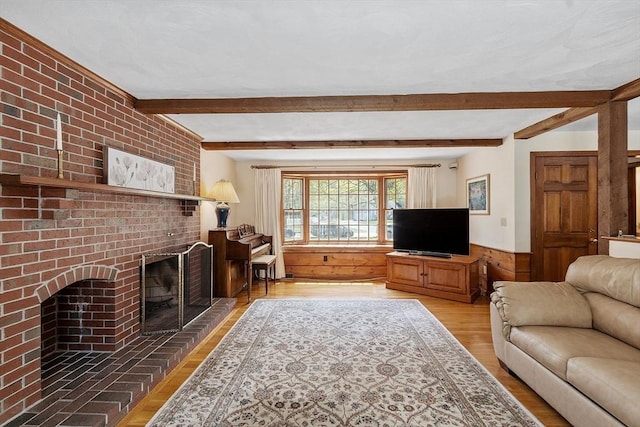 living room with beam ceiling, a brick fireplace, wood walls, a wainscoted wall, and wood finished floors