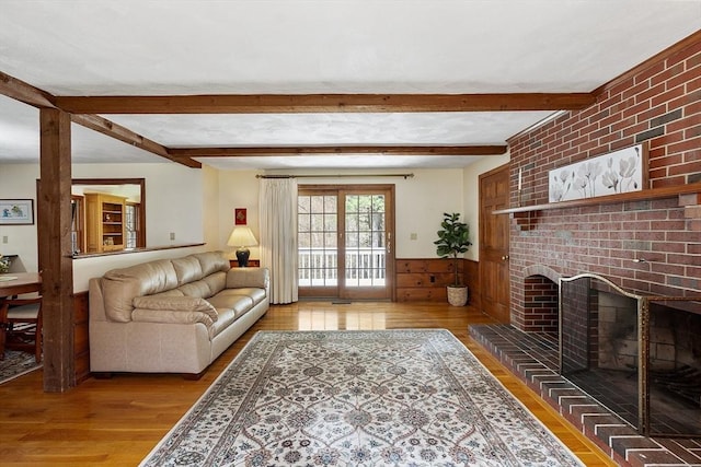 living area featuring beamed ceiling, wood walls, wood finished floors, and a wainscoted wall