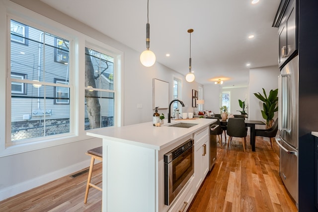 kitchen featuring sink, an island with sink, pendant lighting, and light hardwood / wood-style floors