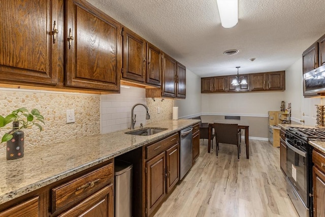 kitchen with light stone counters, stainless steel appliances, sink, light hardwood / wood-style floors, and hanging light fixtures