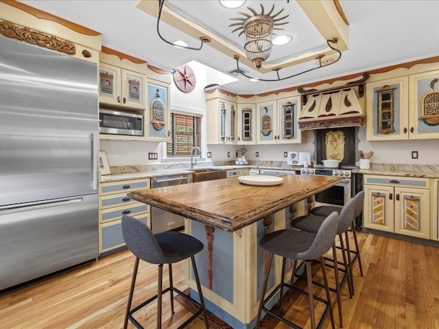 kitchen featuring a kitchen island, sink, built in appliances, a raised ceiling, and custom range hood