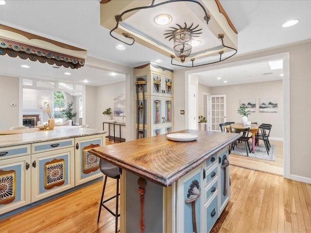 kitchen featuring a kitchen island, a fireplace, white cabinets, a tray ceiling, and light hardwood / wood-style flooring