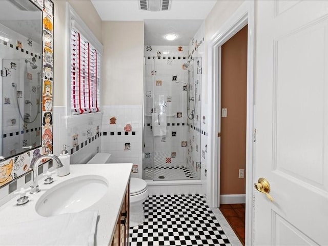 bathroom with vanity, a shower with door, tile walls, and toilet