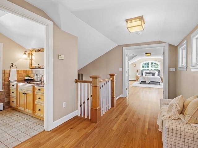 hall featuring lofted ceiling, sink, and light wood-type flooring