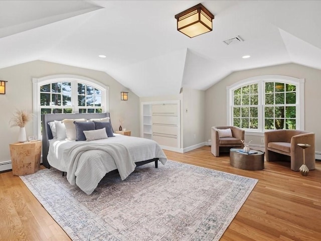 bedroom with vaulted ceiling, a baseboard heating unit, and light hardwood / wood-style floors