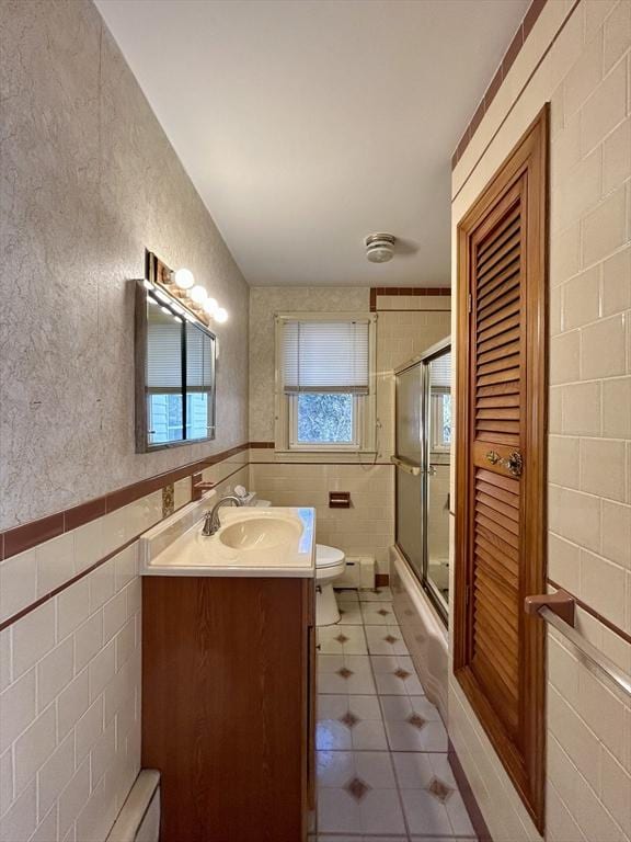 full bathroom with toilet, tile patterned flooring, shower / bath combination with glass door, tile walls, and vanity