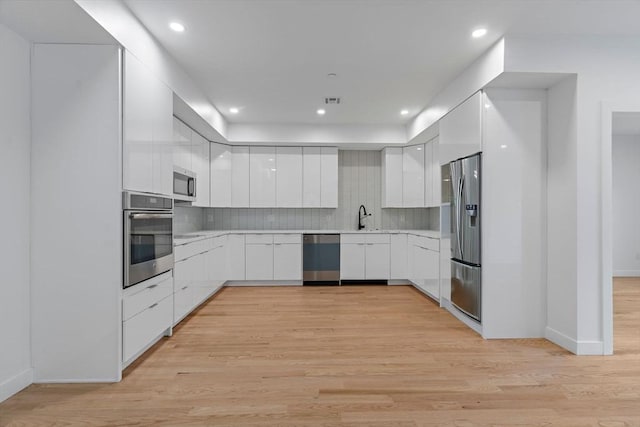 kitchen featuring sink, white cabinets, light hardwood / wood-style floors, backsplash, and appliances with stainless steel finishes