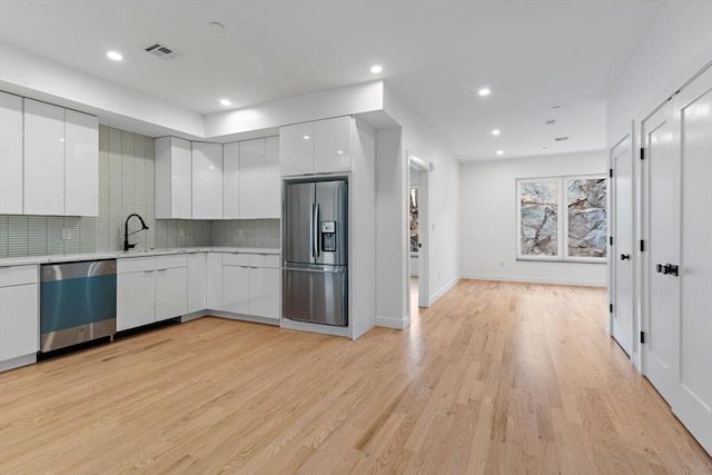 kitchen featuring light hardwood / wood-style flooring, stainless steel appliances, tasteful backsplash, white cabinetry, and sink