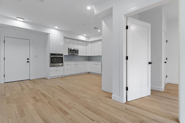 kitchen with appliances with stainless steel finishes, light hardwood / wood-style flooring, white cabinetry, and decorative backsplash