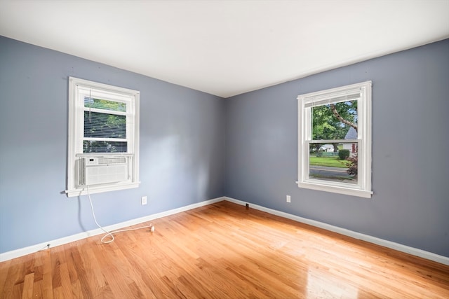 empty room featuring plenty of natural light, cooling unit, and wood-type flooring