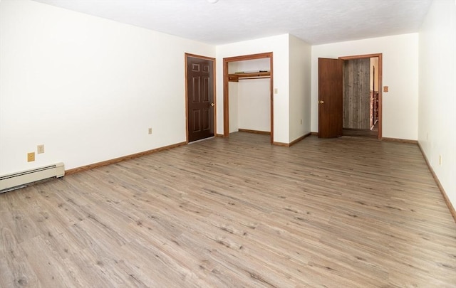 unfurnished bedroom featuring a closet, baseboard heating, and light hardwood / wood-style flooring