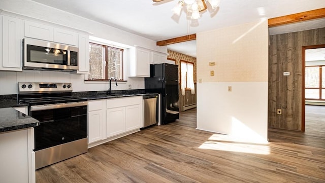 kitchen with sink, white cabinetry, hardwood / wood-style floors, stainless steel appliances, and dark stone counters