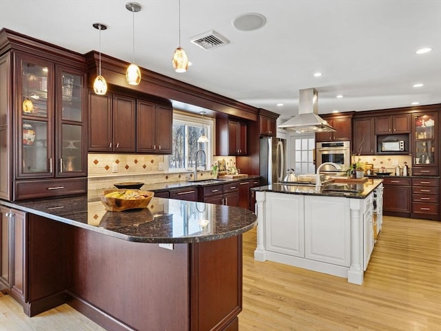 kitchen featuring appliances with stainless steel finishes, dark stone counters, island range hood, and a spacious island