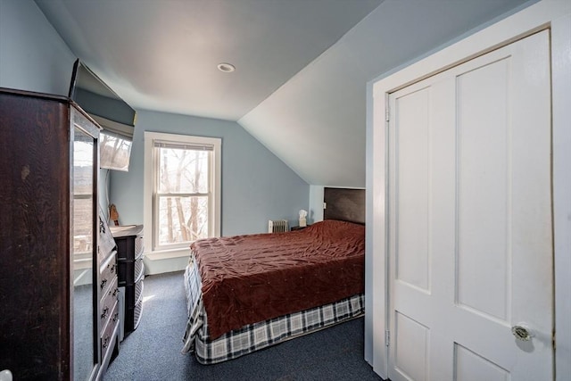 carpeted bedroom with a closet, radiator heating unit, and vaulted ceiling