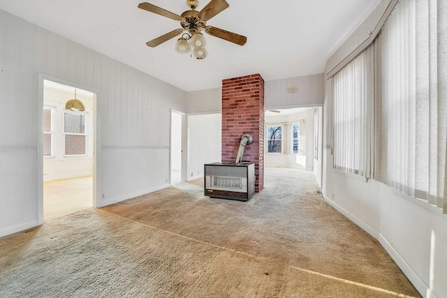 unfurnished living room with ceiling fan, baseboards, a wood stove, and carpet