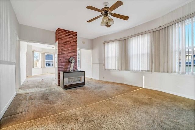 unfurnished living room featuring a wood stove, carpet, baseboards, and ceiling fan