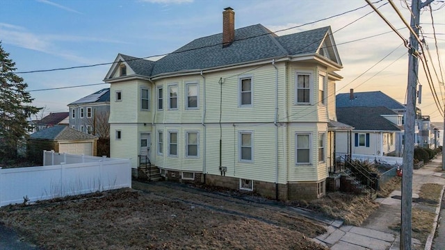 back of property featuring a shingled roof, a chimney, and fence