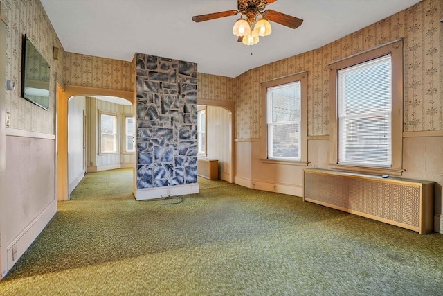 spare room with wallpapered walls, radiator heating unit, carpet flooring, wainscoting, and arched walkways