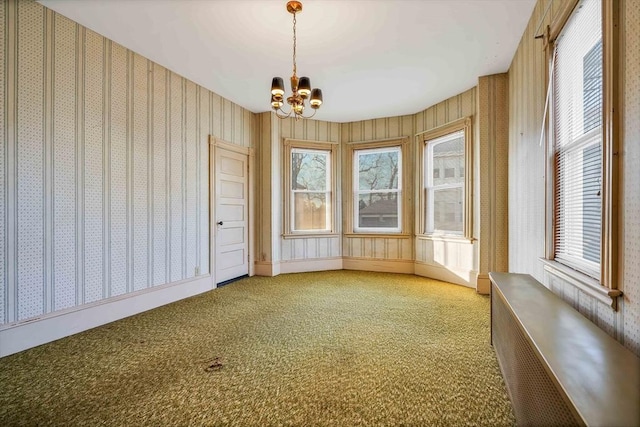 carpeted empty room with wallpapered walls, plenty of natural light, radiator heating unit, and a chandelier