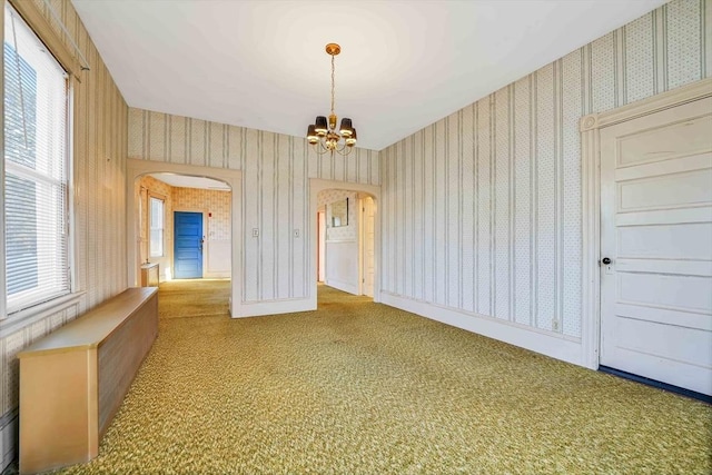 carpeted empty room with arched walkways, a notable chandelier, wallpapered walls, and baseboards