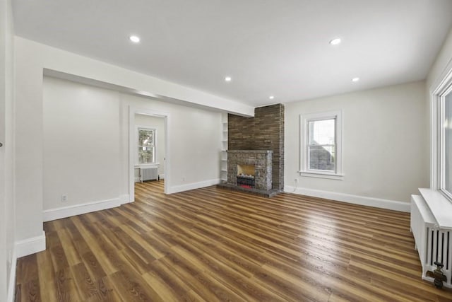 unfurnished living room featuring a stone fireplace, dark hardwood / wood-style floors, and radiator heating unit