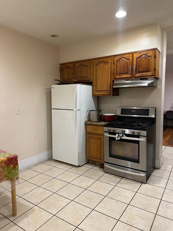 kitchen featuring white fridge, light tile patterned floors, and stainless steel gas range