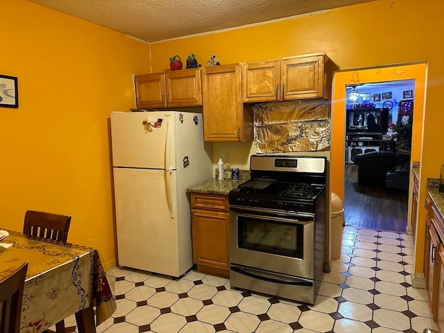 kitchen featuring a textured ceiling, gas stove, white fridge, and dark stone countertops