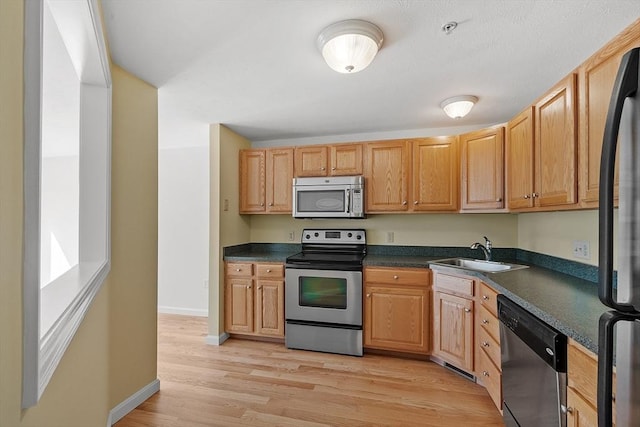 98 Caspian Way Unit 98, Fitchburg, MA 01420 - kitchen with dark countertops, a sink, light wood-style flooring, baseboards, and appliances with stainless steel finishes