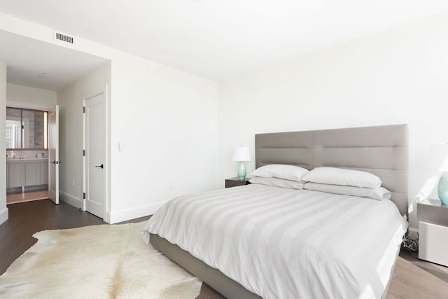 bedroom with ensuite bath and hardwood / wood-style floors