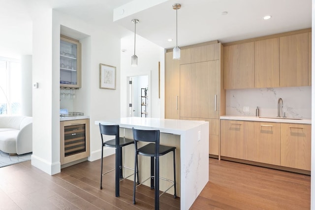 kitchen with pendant lighting, wine cooler, sink, and light hardwood / wood-style floors