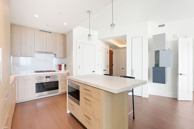 kitchen featuring appliances with stainless steel finishes, a kitchen island, pendant lighting, wood-type flooring, and light brown cabinetry