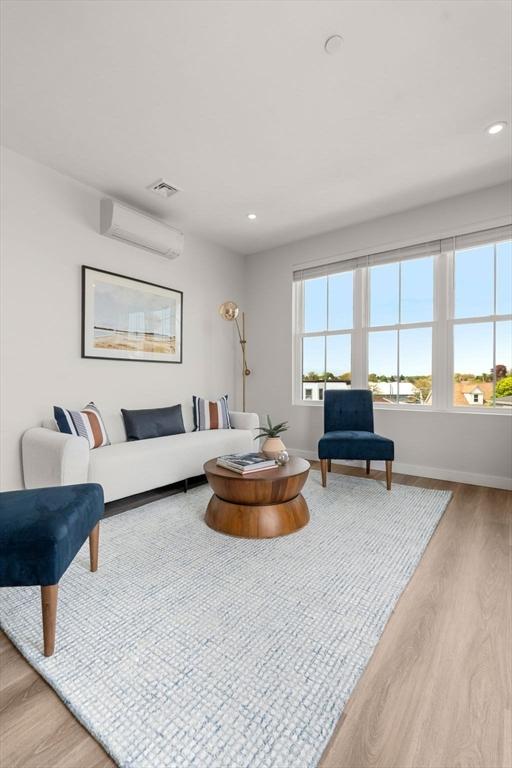 living room featuring an AC wall unit, baseboards, visible vents, and wood finished floors