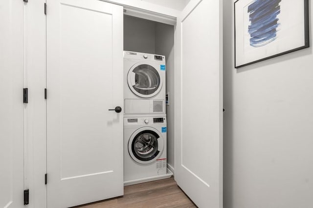 laundry area with stacked washer and clothes dryer, laundry area, wood finished floors, and baseboards