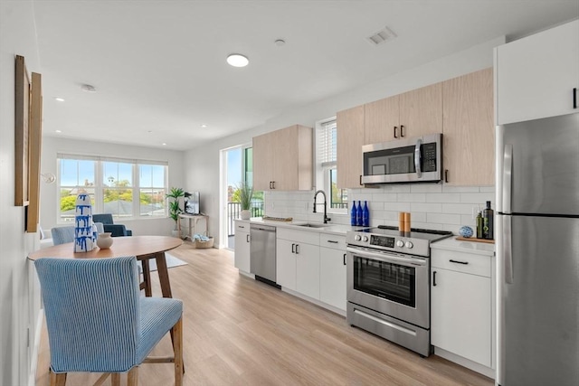 kitchen featuring appliances with stainless steel finishes, a sink, backsplash, light countertops, and light wood-type flooring