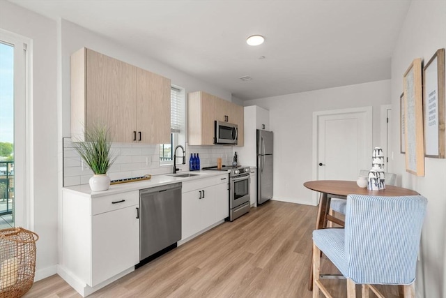 kitchen with light wood-style flooring, a sink, light countertops, tasteful backsplash, and appliances with stainless steel finishes