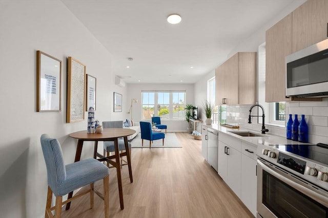 kitchen with light wood finished floors, a sink, light countertops, appliances with stainless steel finishes, and tasteful backsplash