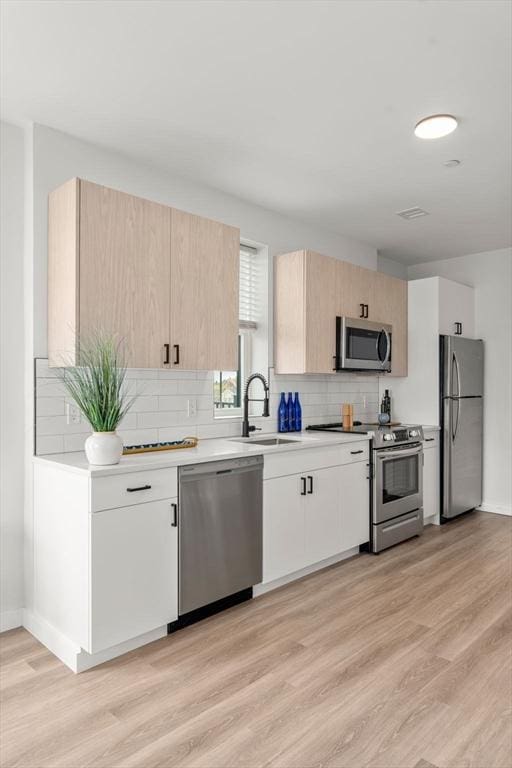 kitchen with light brown cabinetry, stainless steel appliances, a sink, decorative backsplash, and light countertops