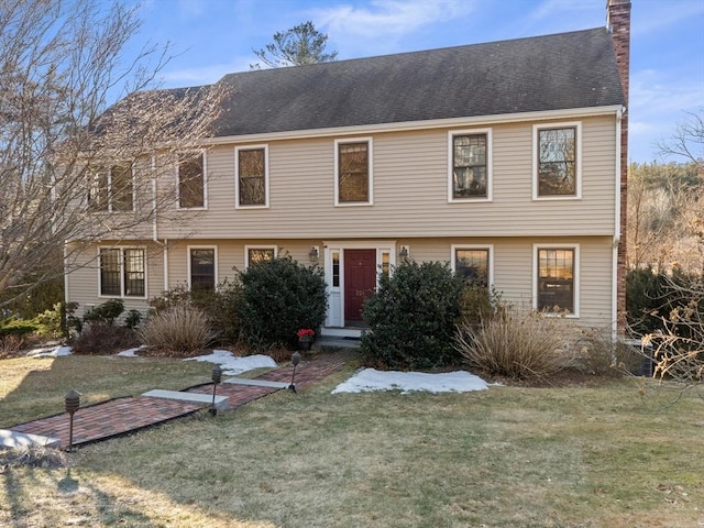 colonial-style house with a chimney, a front lawn, and a shingled roof